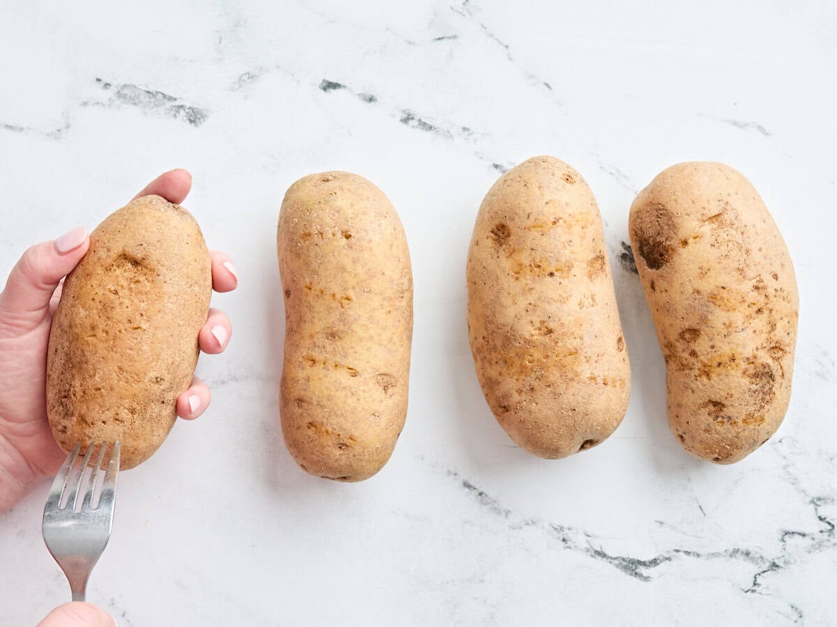 A hand pricking a potato with a fork before baking.