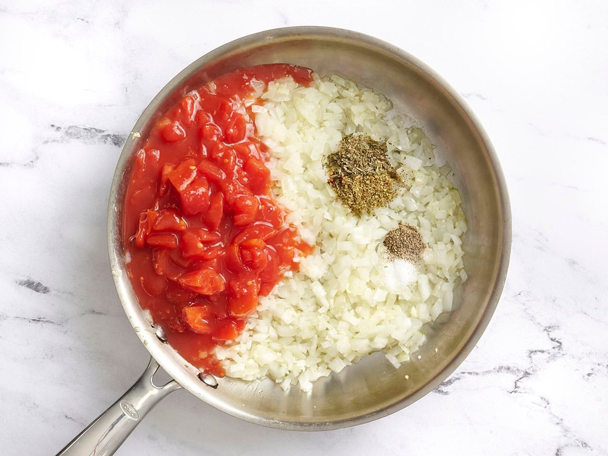 Chopped tomatoes and seasonings added to sauteed onions and garlic in a skillet.