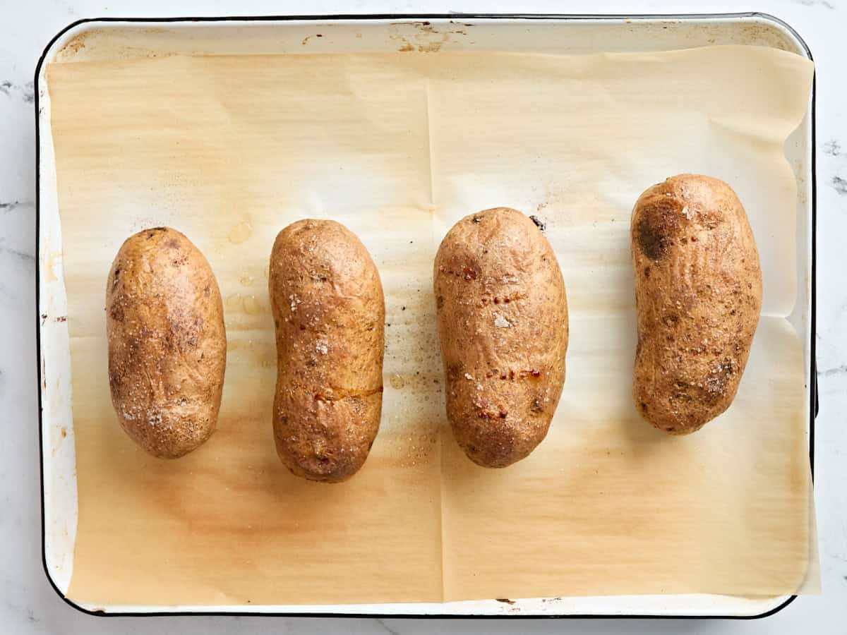 Four baked potatoes on a parchment lined baking sheet.
