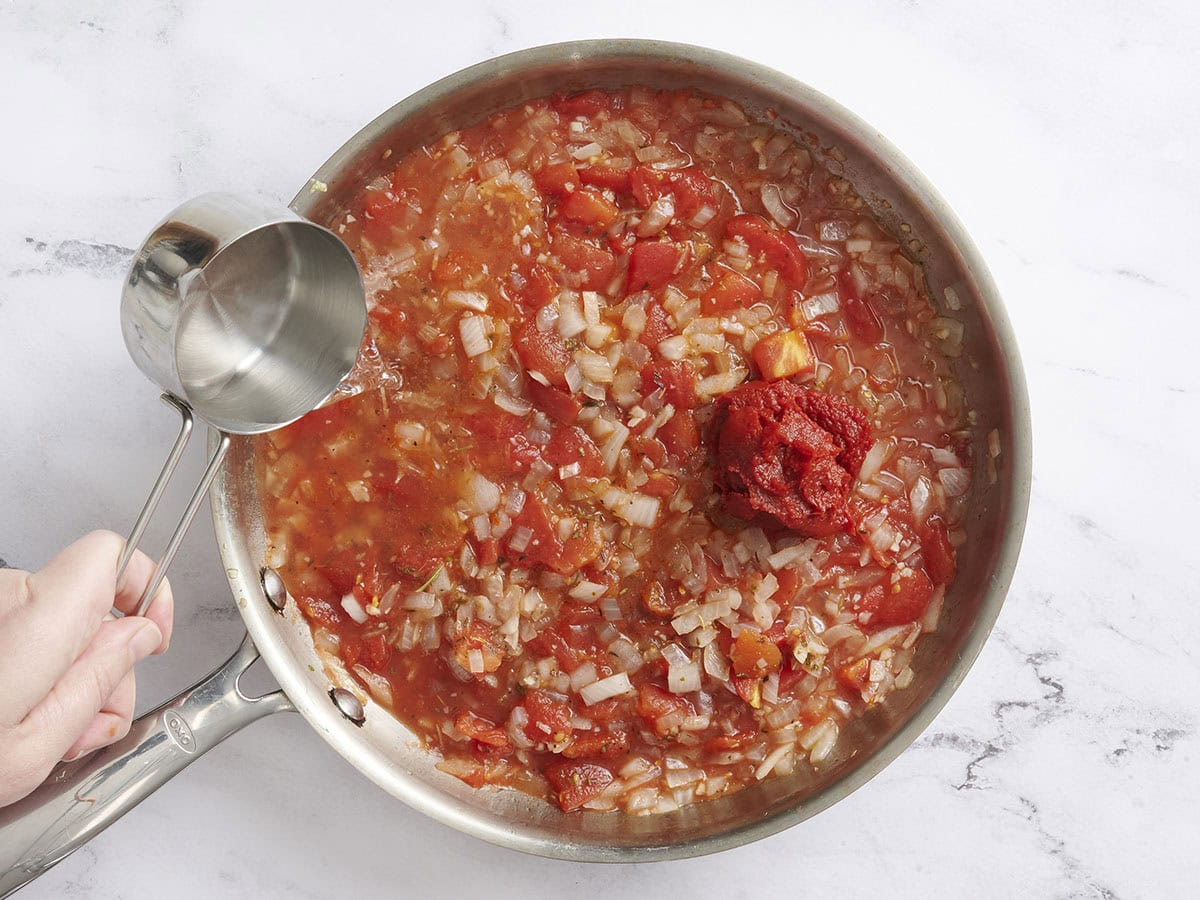 Water and tomato paste added toa skillet of tomato sauce and onions.