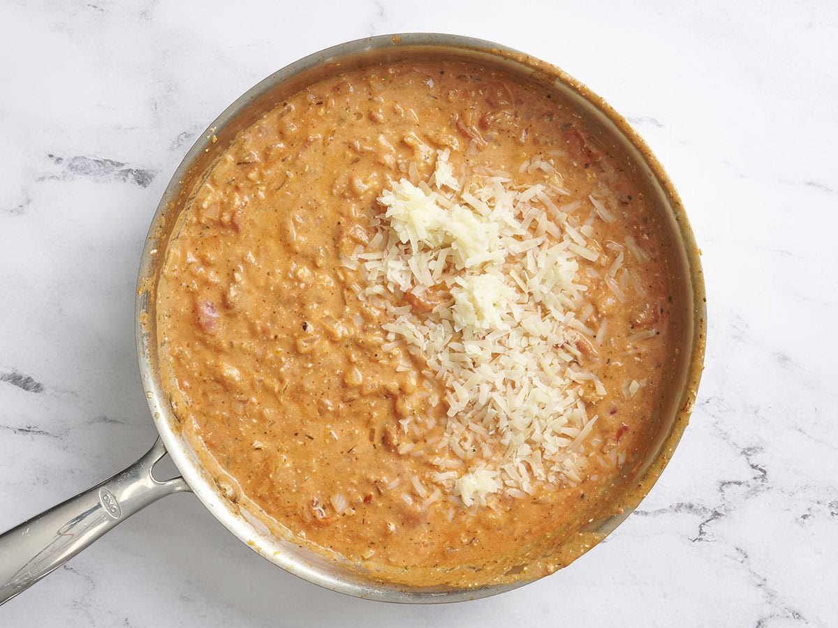 Grated parmesan cheese added to a creamy tomato sauce in a skillet.