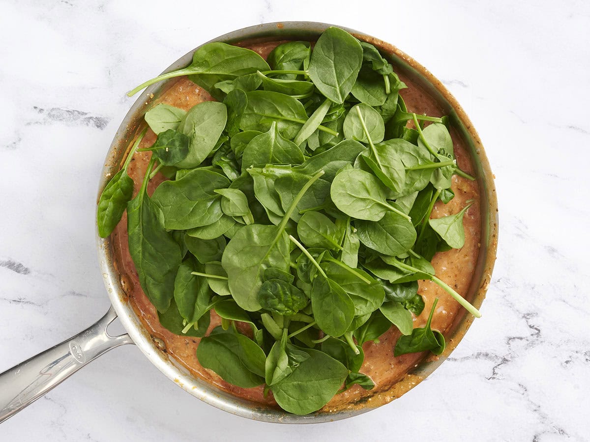 Spinach added to a creamy tomato sauce in a skillet