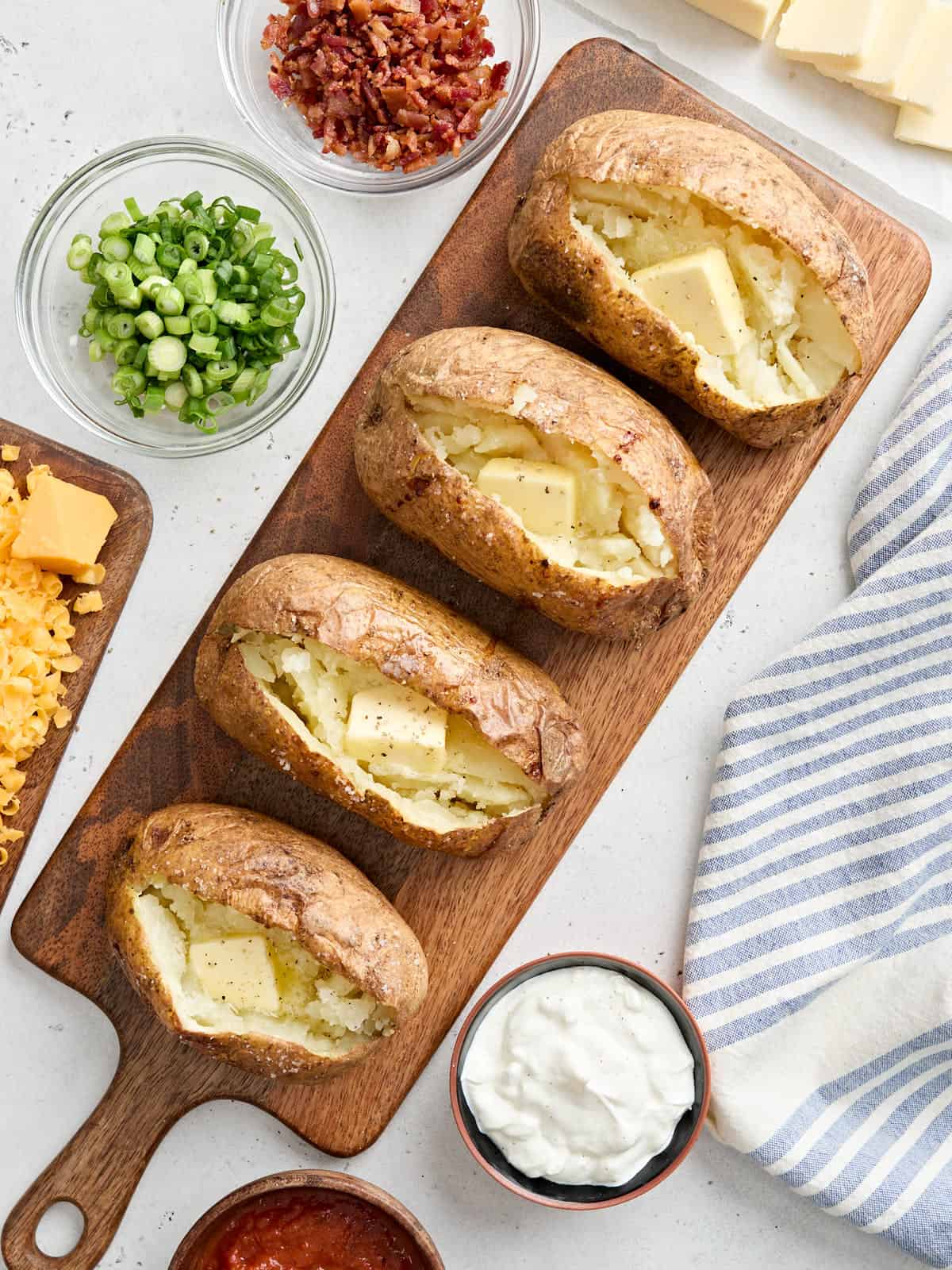 Overhead view of four homemade baked potatoes on a wooden board, topped with butter.