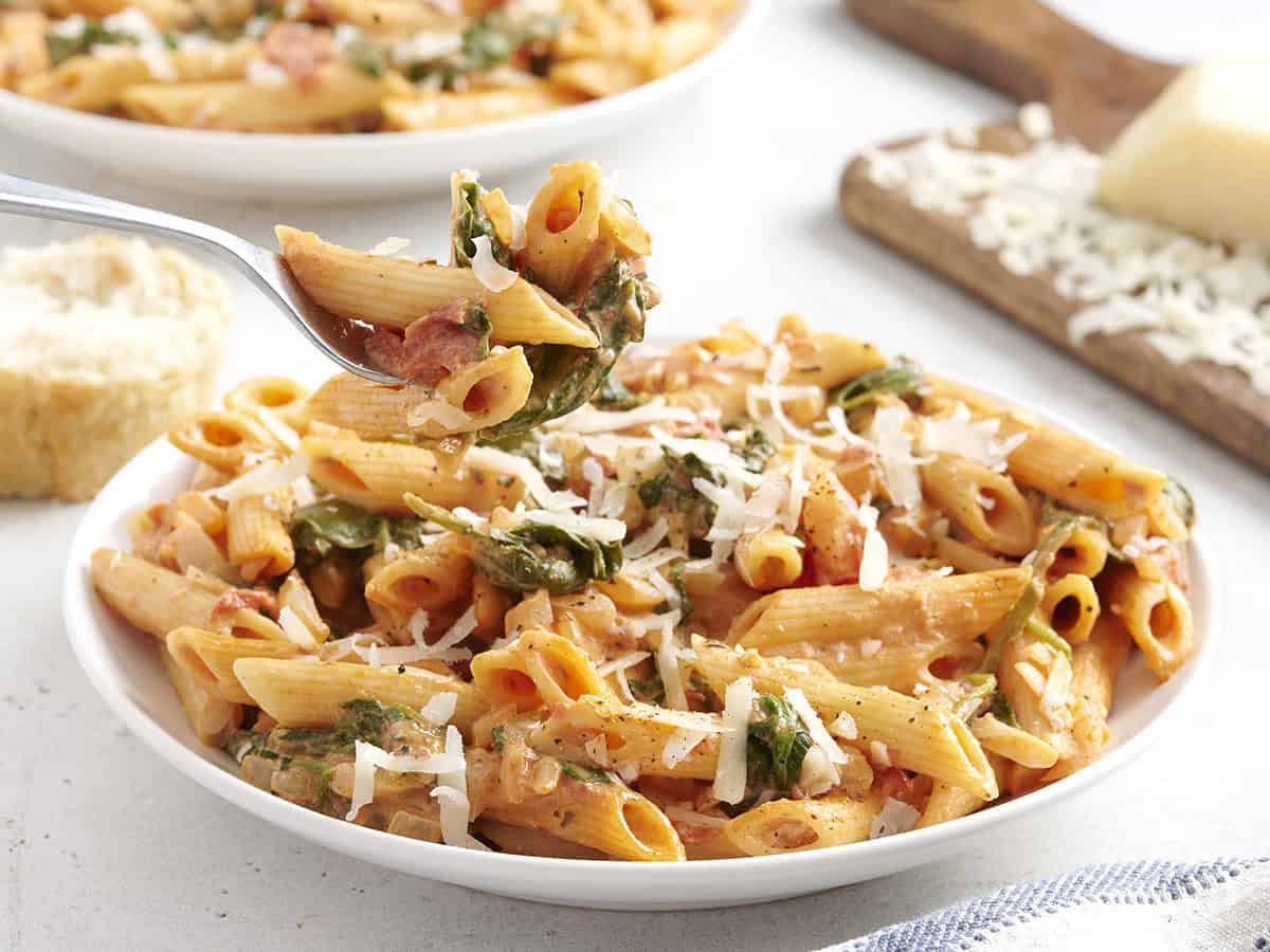 Easier than a box meal, this creamy tomato and spinach pasta is also more flavorful and delicious. 100% real ingredients. Perfect for busy weeknights! Budetbytes.com Side view of tomato spinach pasta on a plate with a fork taking some.
