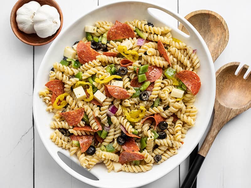 Repurpose your leftover pizza toppings into this deliciously simple Italian style pizza pasta salad. Including a simple homemade Italian dressing! Budetbytes.com Overhead view of pizza pasta salad in a serving bowl with wooden salad utensils on the side
