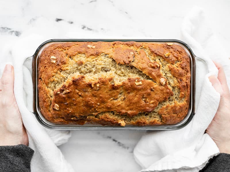 This super moist banana bread recipe uses plain yogurt to keep the bread soft and tender with less butter or oil. Add walnuts or even chocolate! BudgetBytes.com Baked yogurt banana bread being held by two hands with white towels