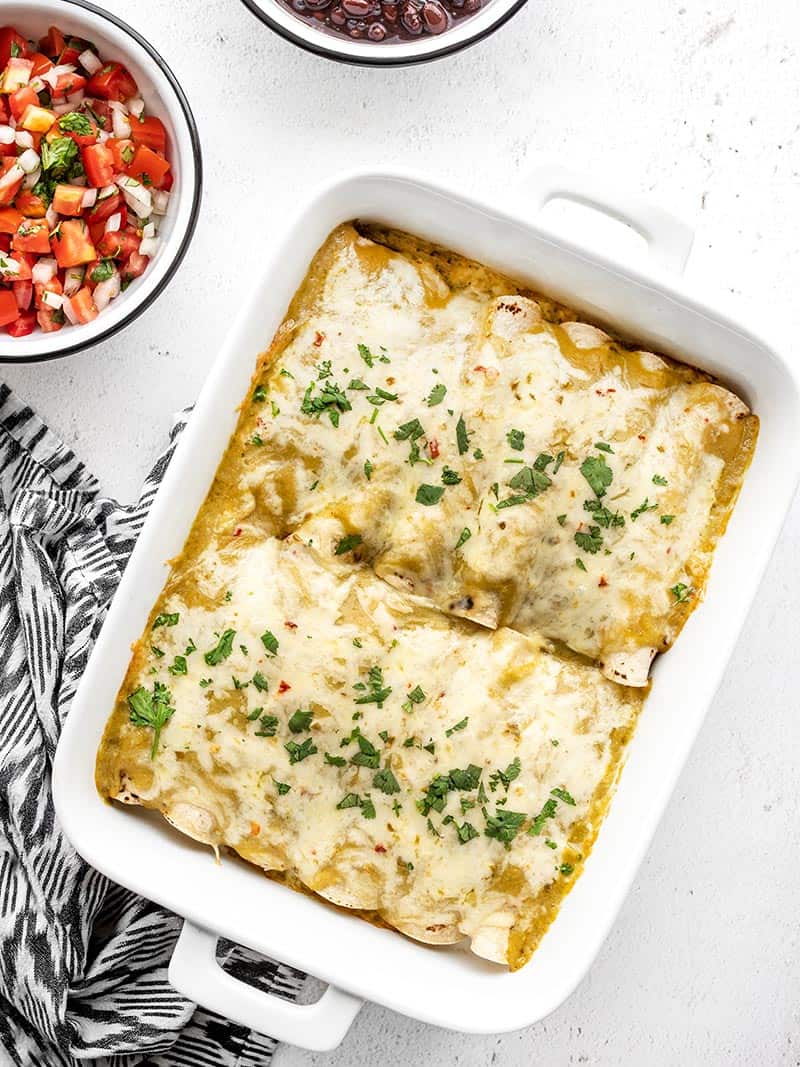 A creamy, cheesy chicken filling inside toasted corn tortillas, smothered with a homemade sauce makes these green chile chicken enchiladas to die for! Budgetbytes.com A casserole dish with green chile chicken enchiladas next to a bowl of pico de gallo