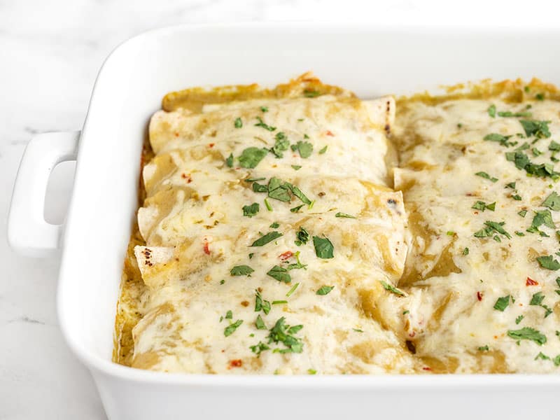 A creamy, cheesy chicken filling inside toasted corn tortillas, smothered with a homemade sauce makes these green chile chicken enchiladas to die for! Budgetbytes.com Side view of the casserole dish full of green chile chicken enchiladas