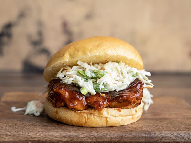 These Easy BBQ Chicken Sandwiches are a fast, easy, and delicious way to satisfy your BBQ craving. No grill needed! Perfect for busy weeknights. Budgetbytes.com Front view of a single Easy BBQ Chicken Sandwich on a wooden cutting board