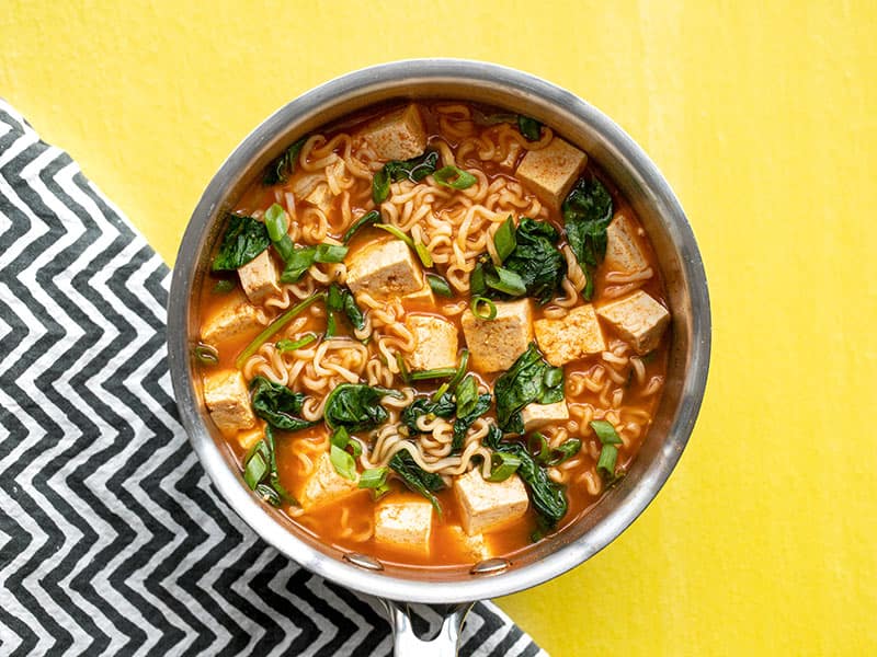 Spicy gochujang gives this instant ramen extra oomph! Gochujang Ramen with Tofu is a quick and easy way to satisfy that noodle craving. Budgetbytes.com Gochujang ramen with tofu in the sauce pot on a yellow background with a black and white zig-zag napkin.