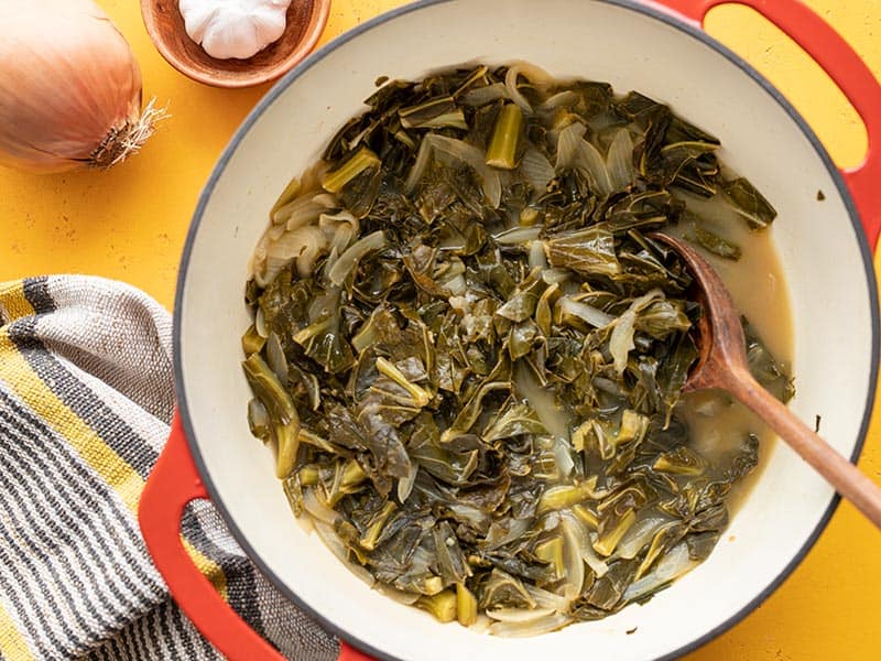 Sweet, spicy, and savory, these Jerk Seasoned Collard Greens are a hearty and flavorful side dish that also makes great leftovers! Budgetbytes.com Jerk seasoned collard greens in a red pot, onion and garlic on the side