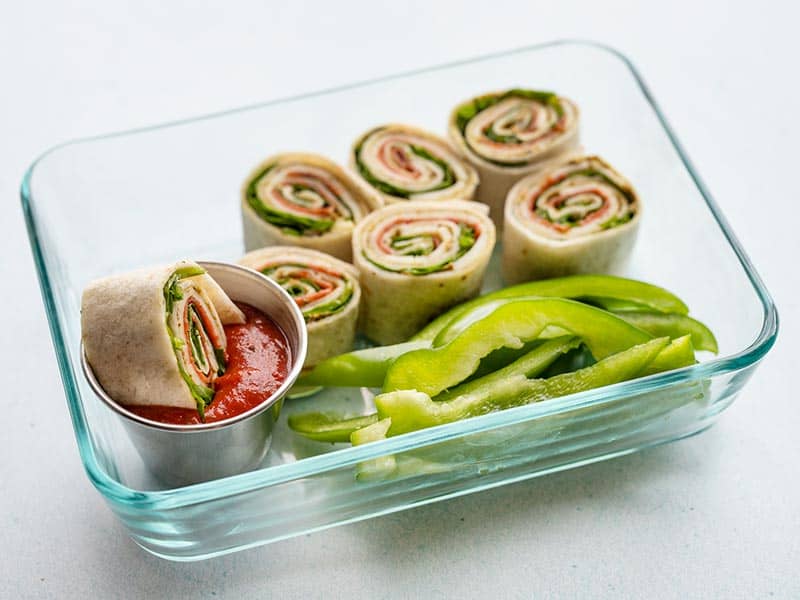 These easy pizza roll up lunch boxes are a great no-cook lunch idea for your work week. No reheating required for this lunch meal prep! Budgetbytes.com A pizza roll up being dipped into a small cup full of pizza sauce