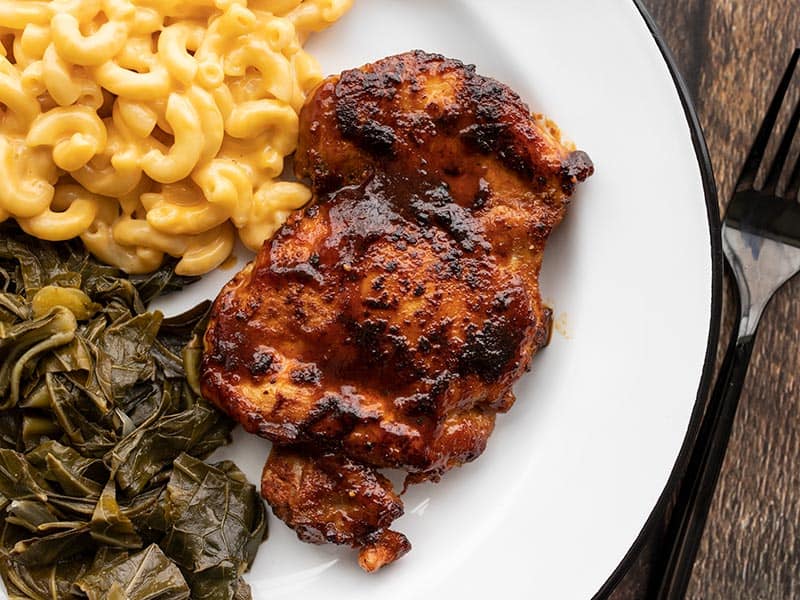 This Quick BBQ Chicken is an easy and tasty main dish that cooks up in under 30 minutes and can be paired with any number of sides. Perfect for weeknights! Budgetbytes.com BBQ chicken thigh on a plate with mac and cheese and collard greens