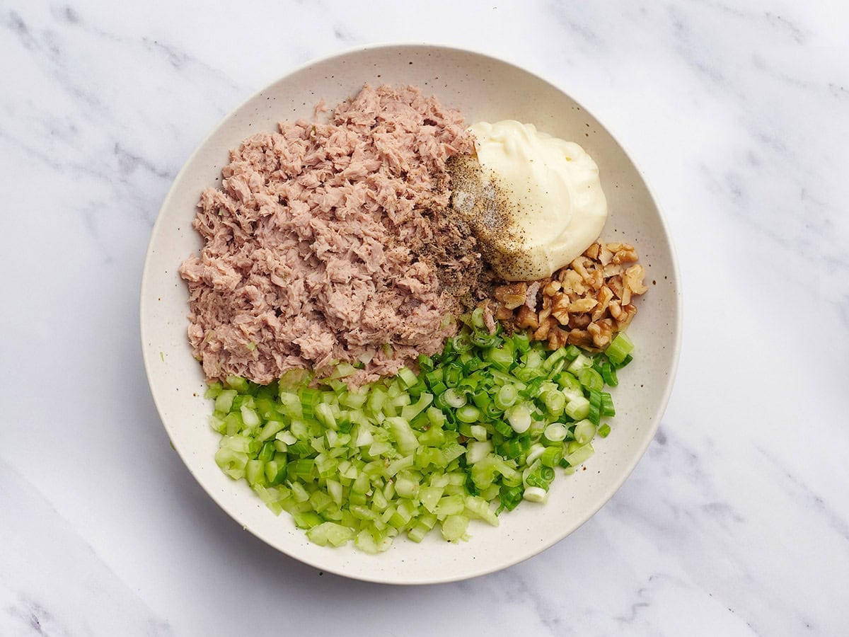 Chopped celery, sliced green onion, diced walnuts, canned tuna and mayo in a bowl.