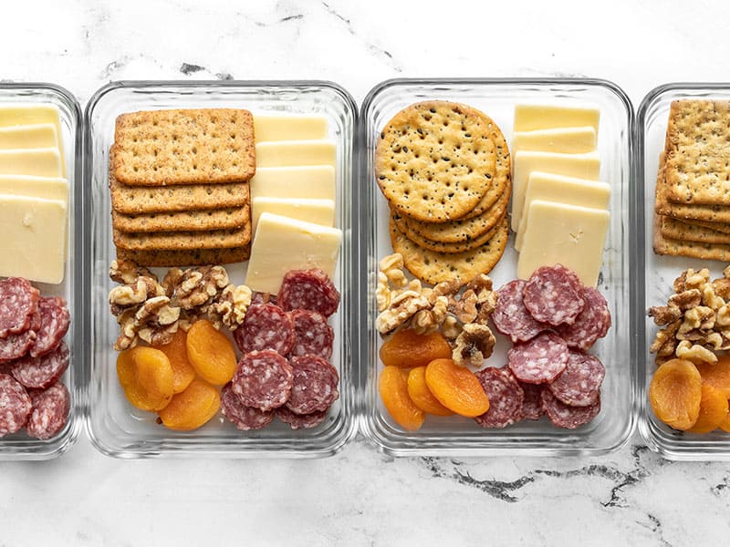 This easy no-cook lunch idea is perfect for the cheese lovers of the world! The Cheese Board Lunch Box makes a meal out of savory nibbles. Budgetbytes.com Four cheese board lunch boxes lined up in a row