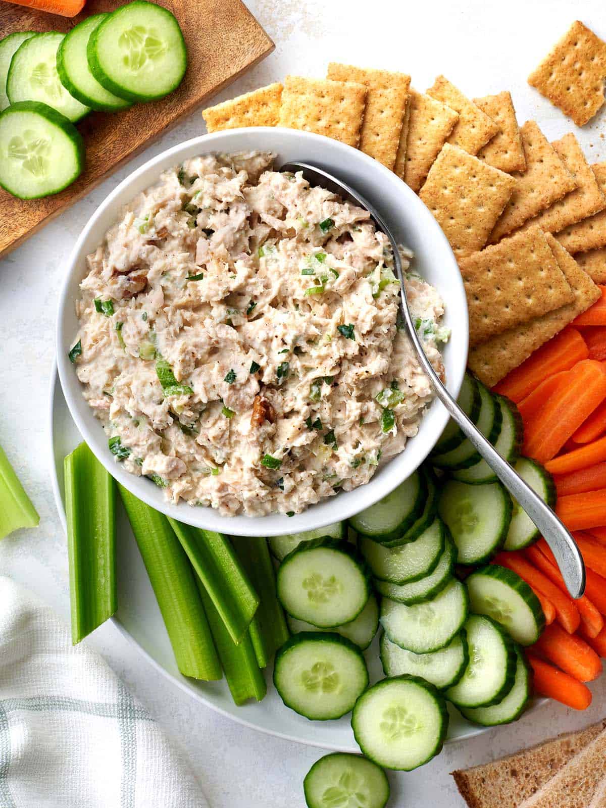 Overhead view of a bowl of homemade tuna salad surrounded by crudites and crackers.
