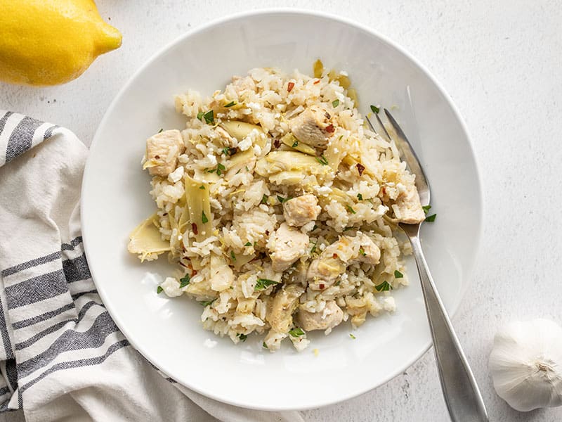 Get back into routines with this easy One Pot Lemon Artichoke Chicken and Rice dinner. 30 minutes, one pot, and you're done! Budgetbytes.com A bowl of one pot lemon artichoke chicken and rice with a fork in the side