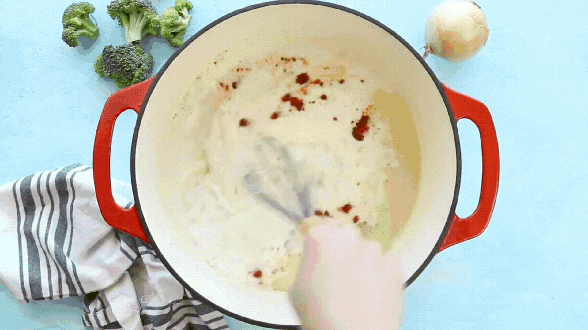 A video GIF showing chopped broccoli being poured into a pot of cheese soup.