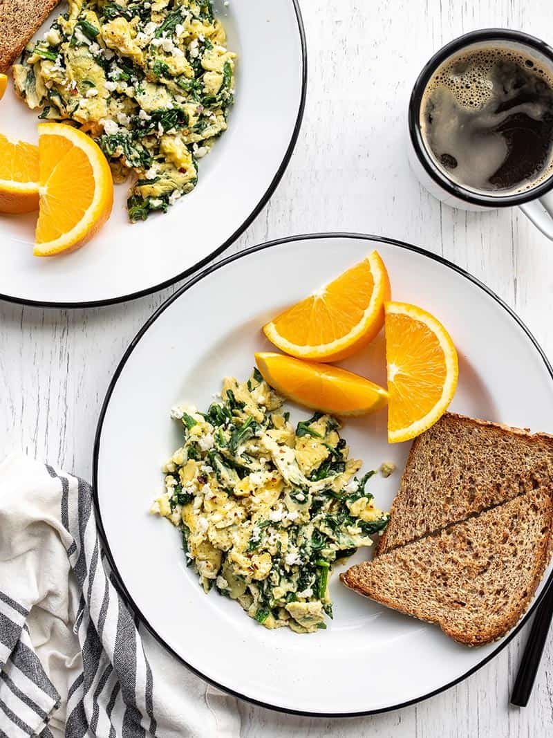 These tasty scrambled eggs with spinach and feta are fast and easy enough to prepare on a weekday, and are perfect for using up spinach! Budgetbytes.com Two plates with scrambled eggs with spinach and feta, toast, and orange slices
