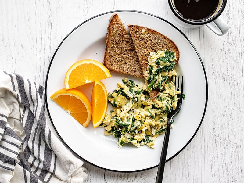 These tasty scrambled eggs with spinach and feta are fast and easy enough to prepare on a weekday, and are perfect for using up spinach! Budgetbytes.com Scrambled eggs with spinach and feta on a plate with toast, half piled onto a slice of toast