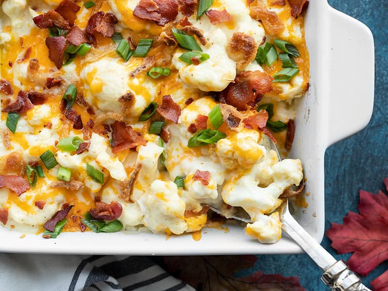 This rich and cheesy loaded cauliflower casserole is an indulgent Thanksgiving side dish with plenty of flare. Budgetbytes.com close up of cheesy loaded cauliflower casserole being scooped out of the dish
