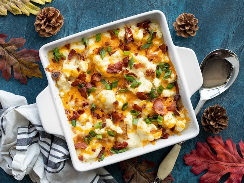 This rich and cheesy loaded cauliflower casserole is an indulgent Thanksgiving side dish with plenty of flare. Budgetbytes.com Overhead view of cheesy loaded cauliflower casserole on a blue background
