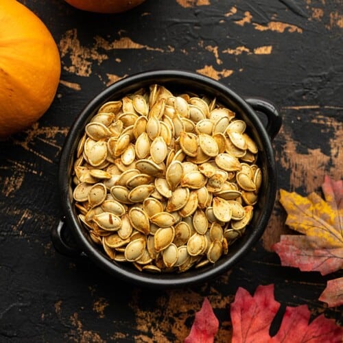 Overhead view of a bowl full of roasted pumpkin seeds on a wooden background.