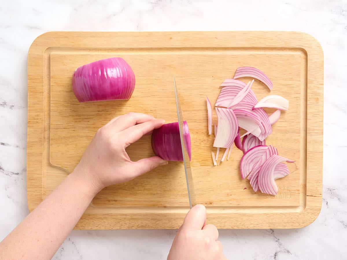 A red onion being sliced on a wooden cutting board.