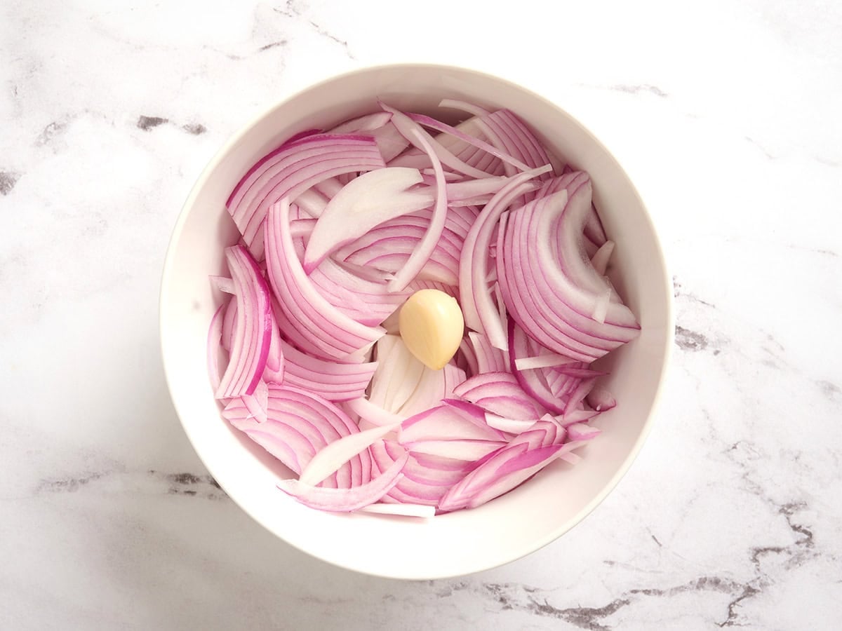 Sliced red onions and garlic in a bowl.