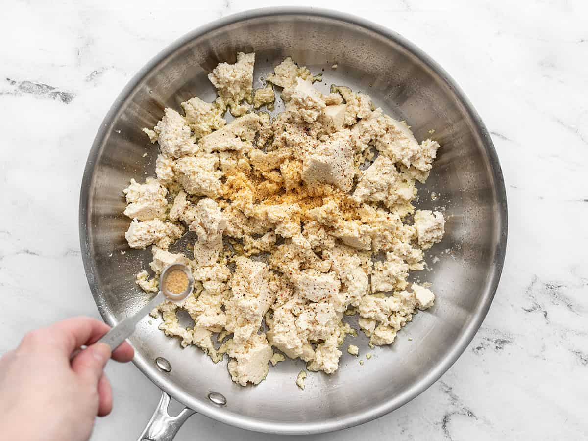 Crumbled tofu in a skillet being seasoned with garlic powder