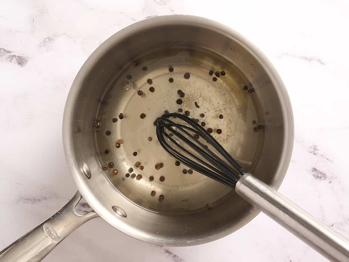 Vinegar in a saucepan with peppercorns.