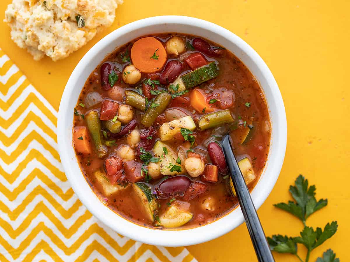 Overhead view of a bowl of vegetarian minestrone with a spoon in the middle