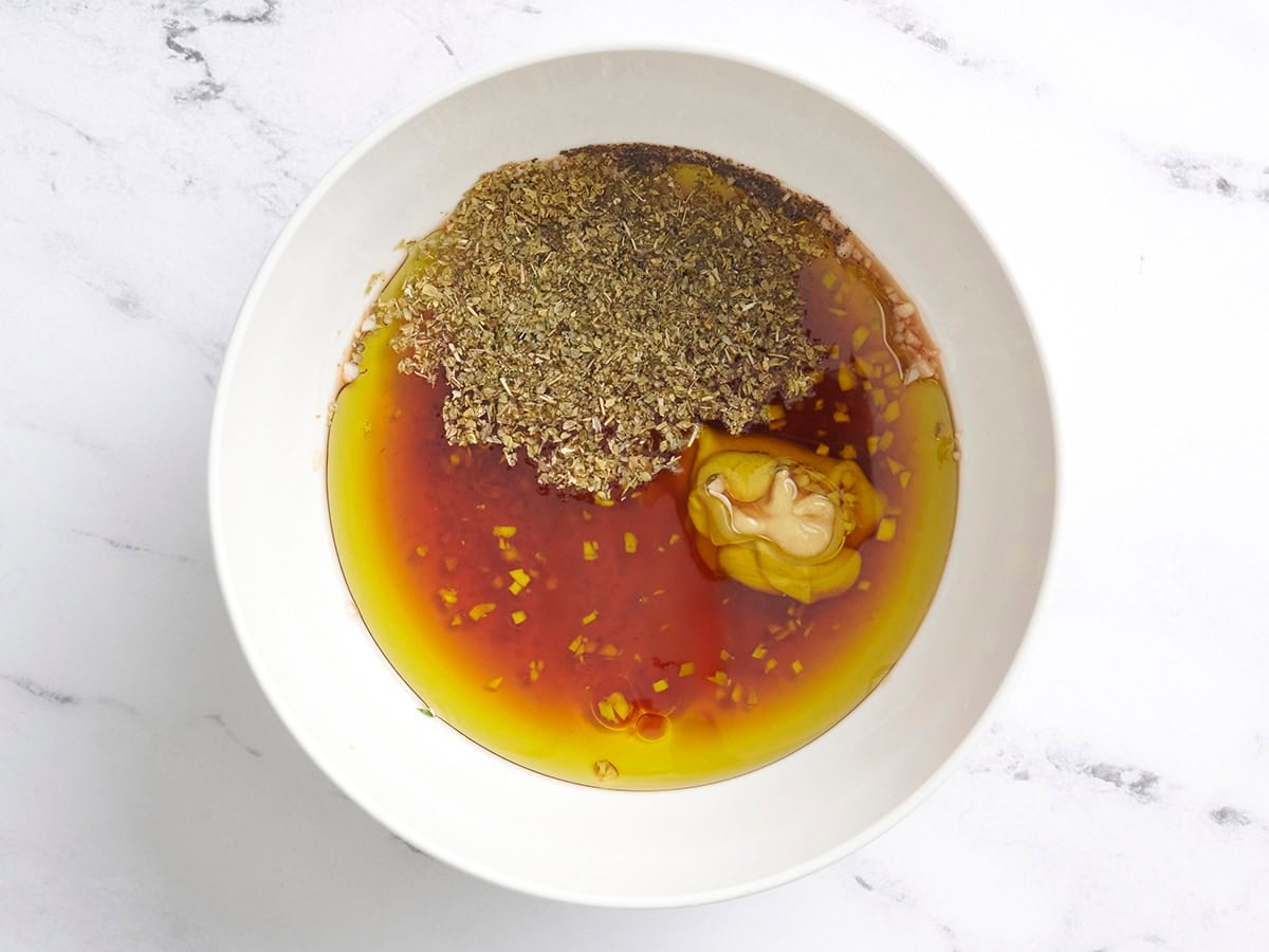 Olive oil, red wine vinegar, dijon mustard, oregano, minced garlic, salt, and pepper in a bowl.