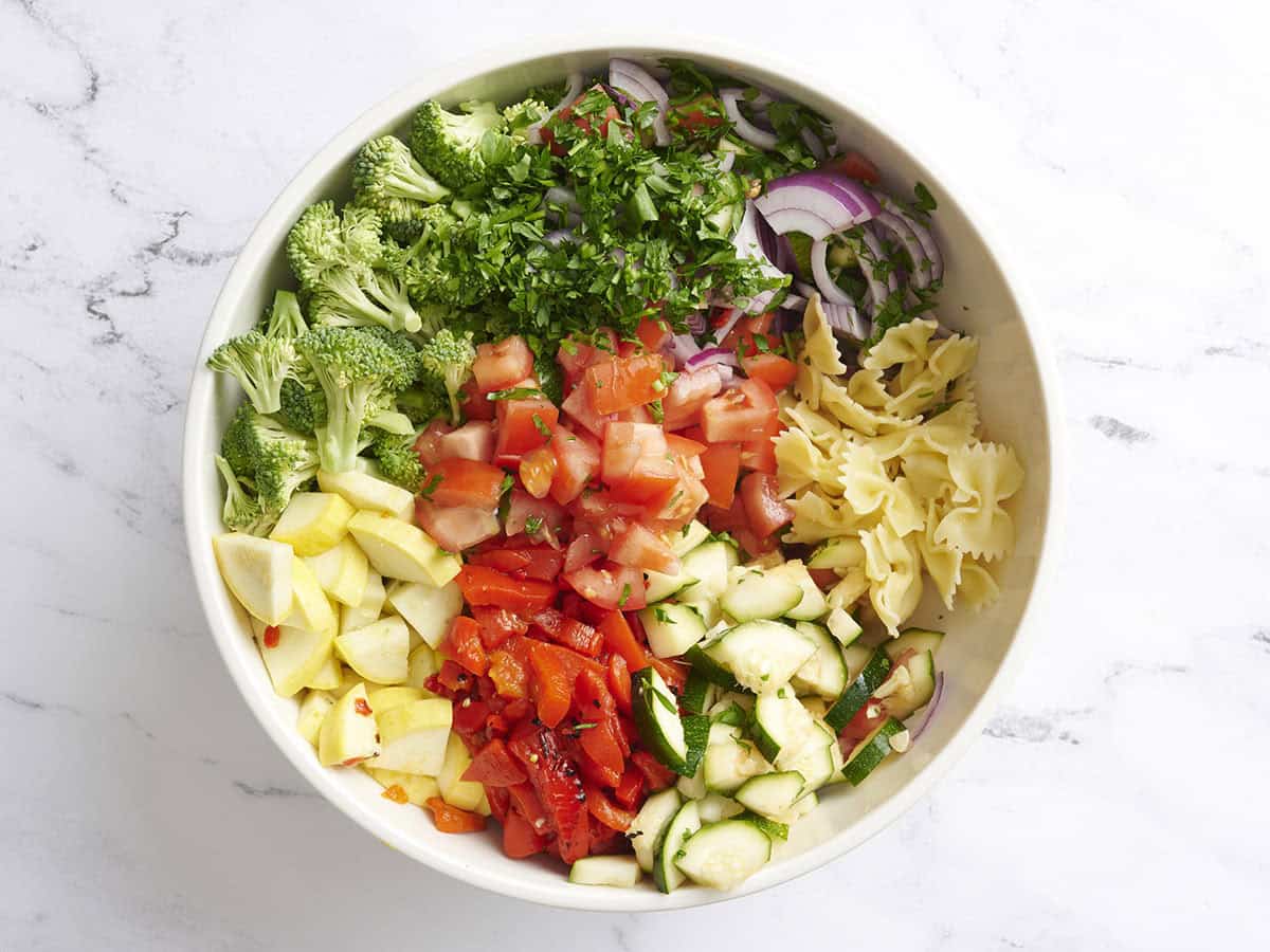 Chopped tomatoes, squash, zucchini, broccoli cooked pasta and parsley in a bowl.