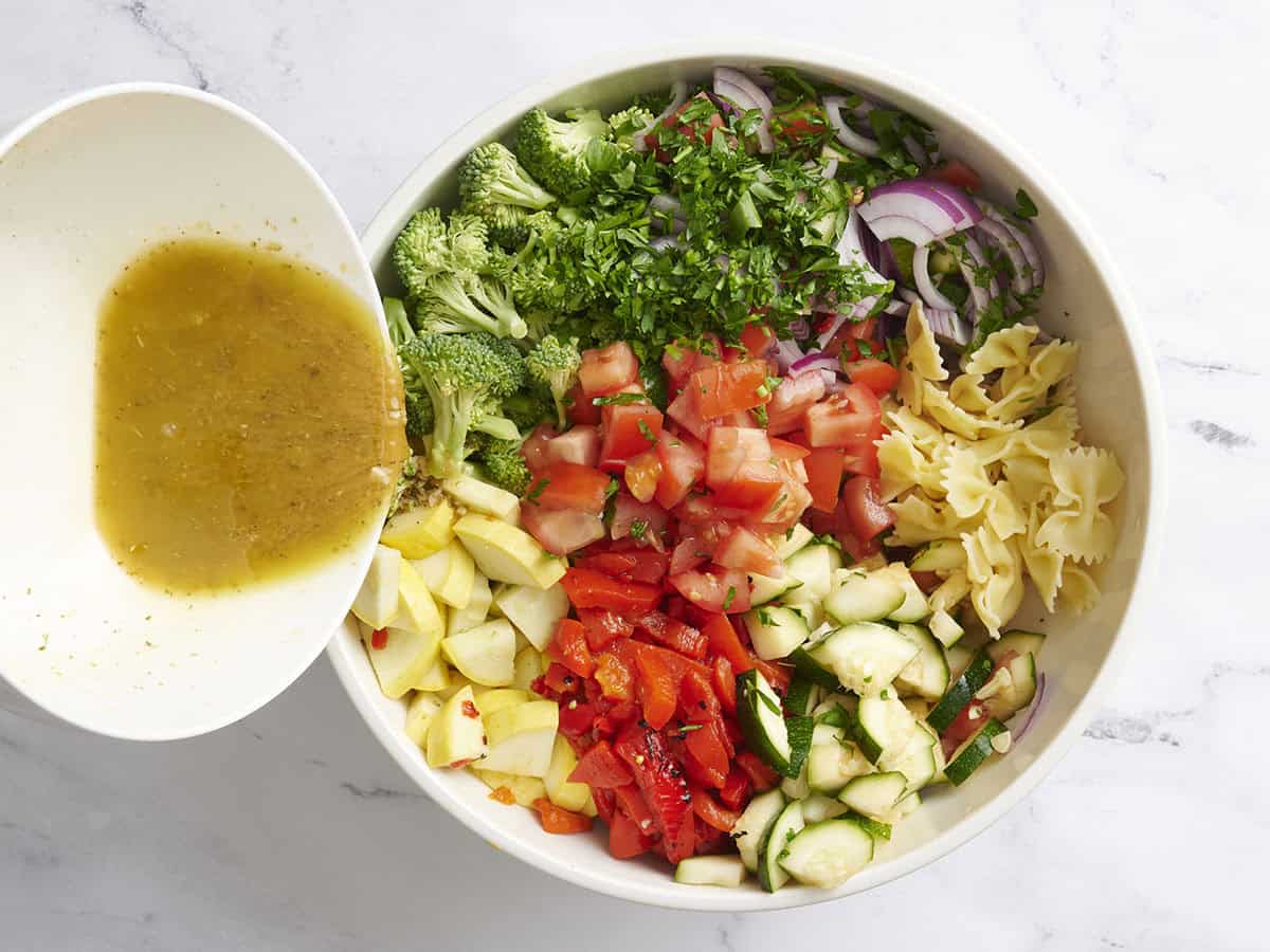 The dressing being added to the ingredients for summer vegetable pasta salad.