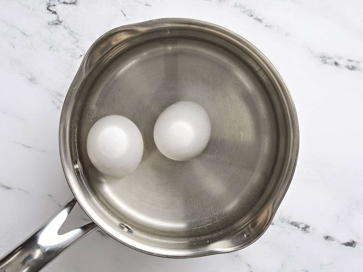 Two boiled eggs in a pan of water.