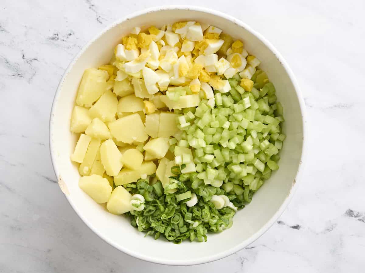 Diced cooked potatoes, chopped boiled eggs, diced celery, and sliced green onions in a mixing bowl.