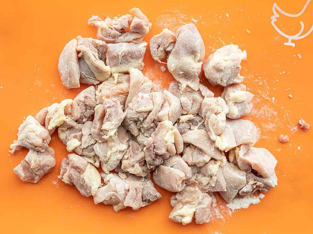 Flour coated chicken thigh pieces on a cutting board.