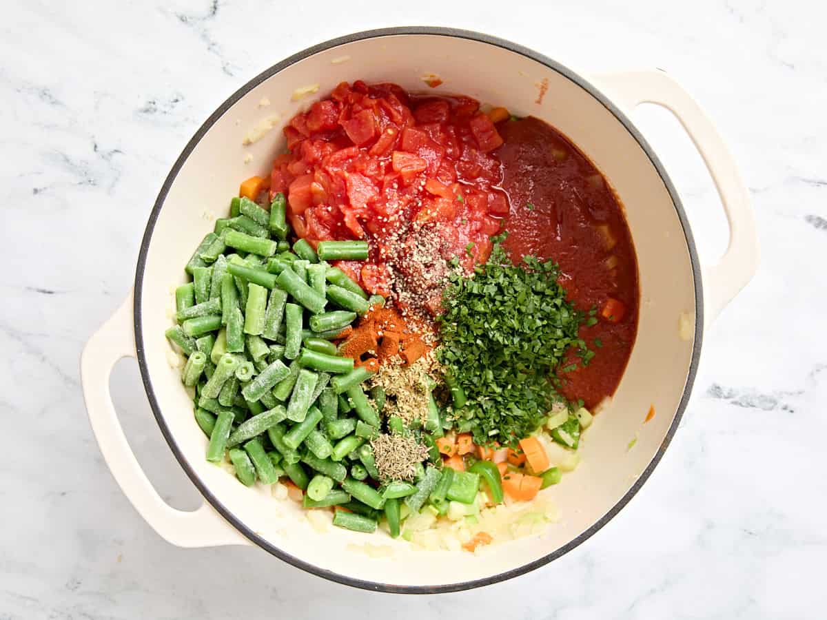 Frozen green beans, canned tomatoes, tomato sauce, and seasonings added to a mirepoix in a sauce pot.