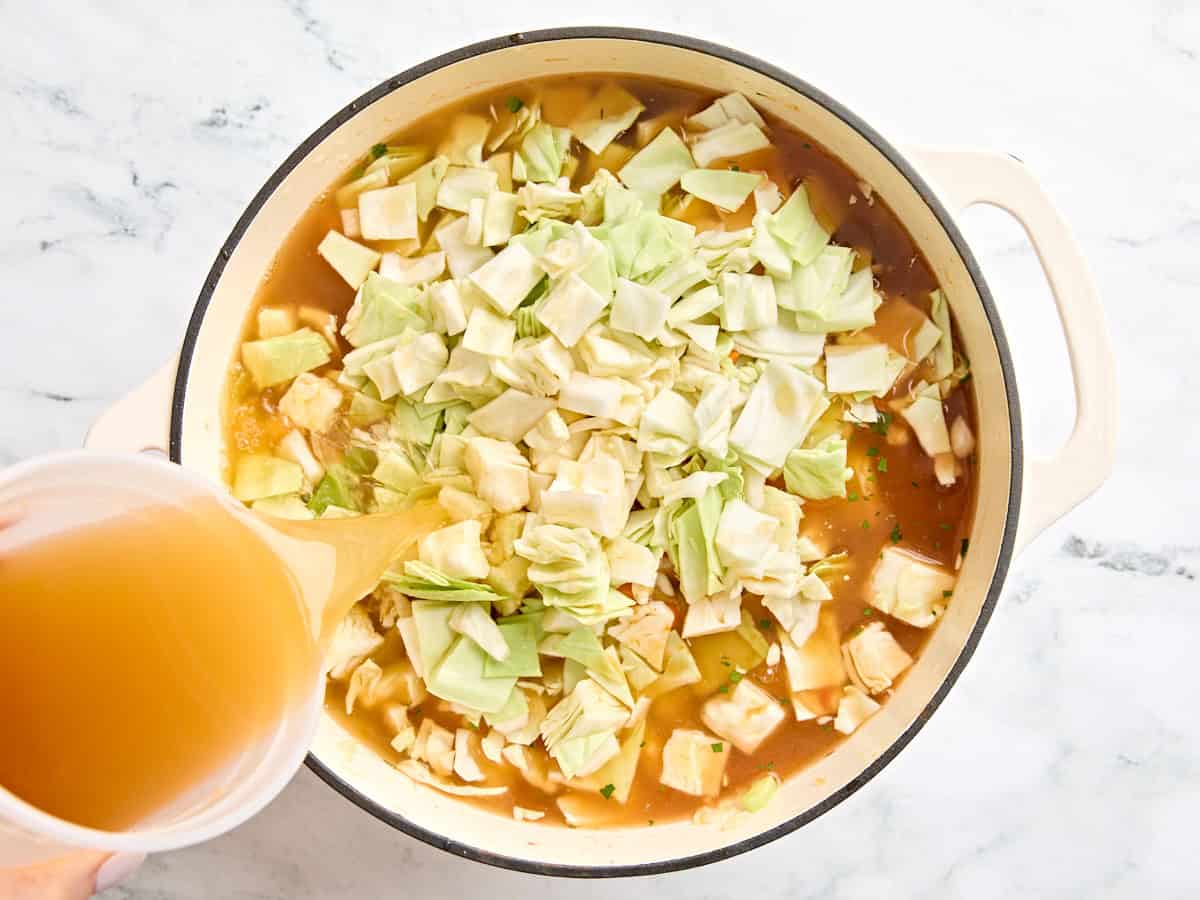 Chopped cabbage and broth added to a soup pot.