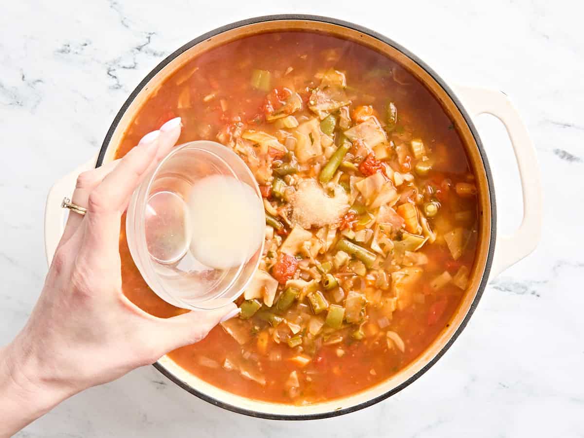 Lemon juice being poured into a pot of cabbage soup.