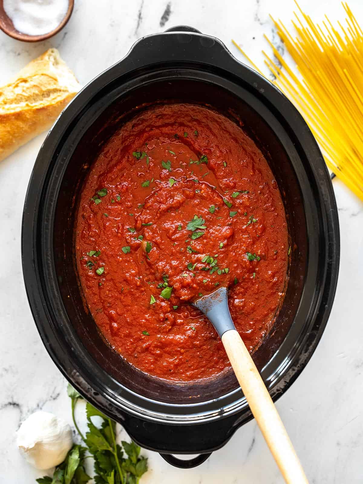 Pasta sauce in a slow cooker with a spoon, garnished with parsley