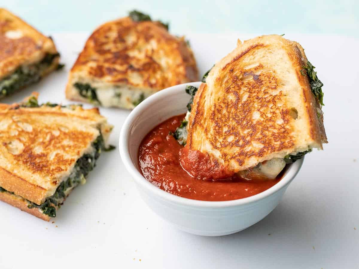 Half of a spinach and feta grilled cheese dipping into pizza sauce.