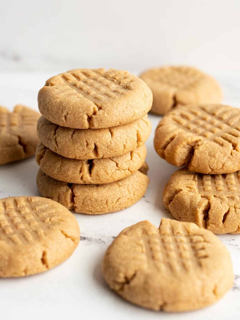 A stack of peanut butter cookies with a few scattered around.
