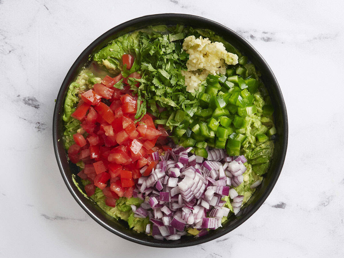 Red onion, chopped cilantro, tomatoes, green bell pepper, and garlic added to mashed avocado.