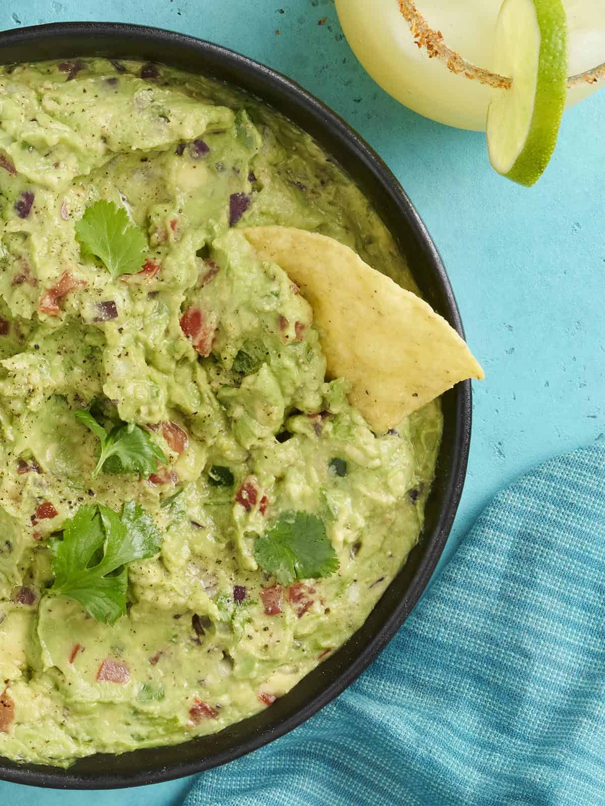 Overhead close up view of a bowl of guacamole with a chip dipped in it.