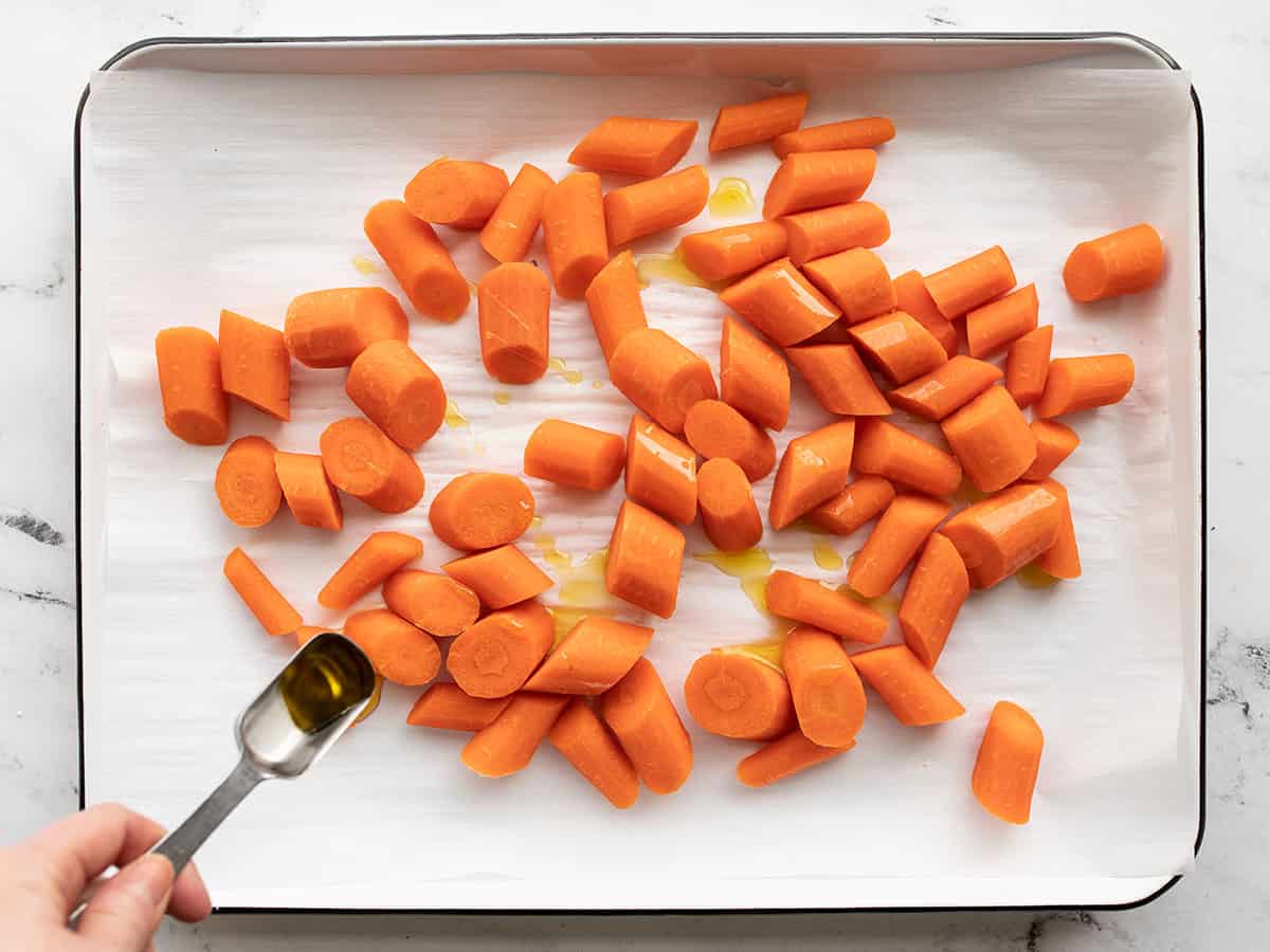 Oil being drizzled over carrots on a baking sheet.