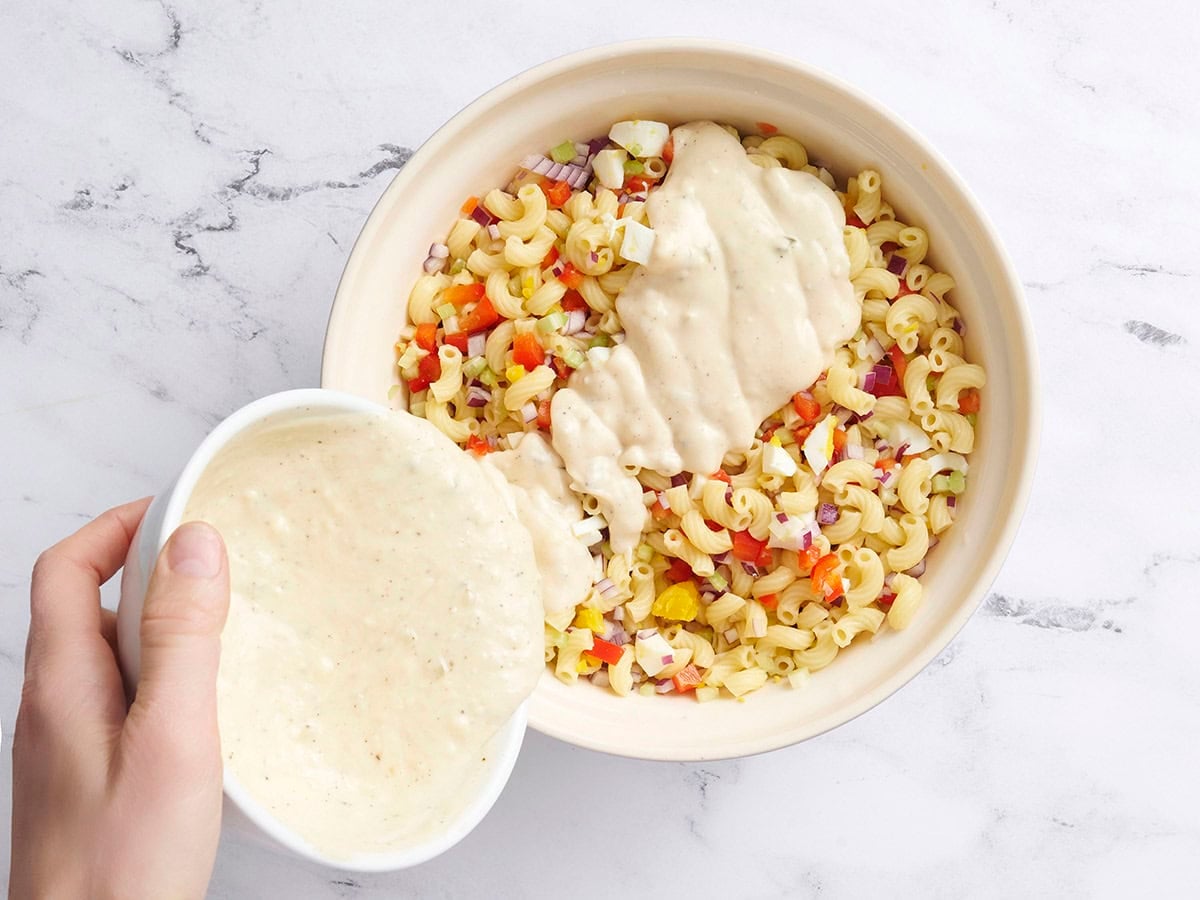 Homemade dressing added to a bowl of macaroni salad.