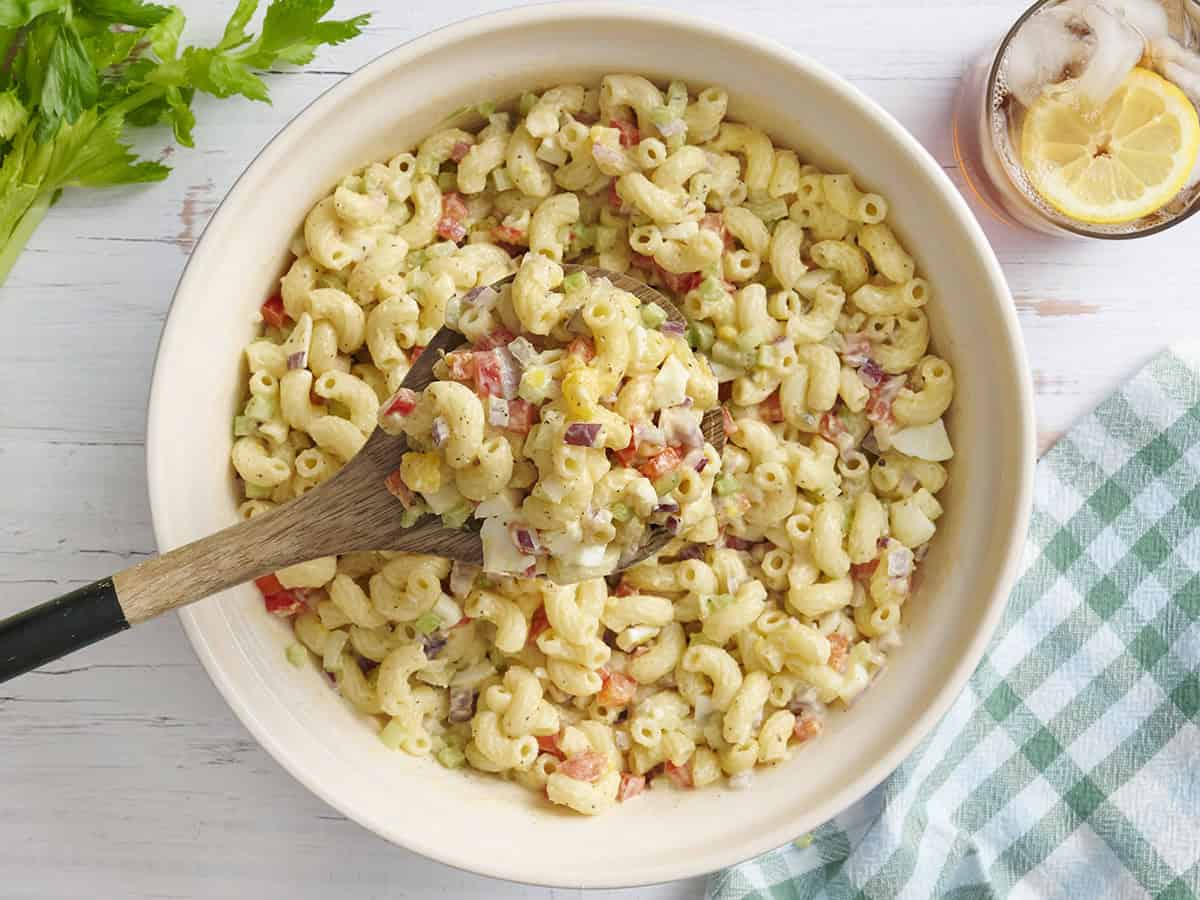 Overhead view of a bowl of macaroni salad with a wooden spoon taking some.
