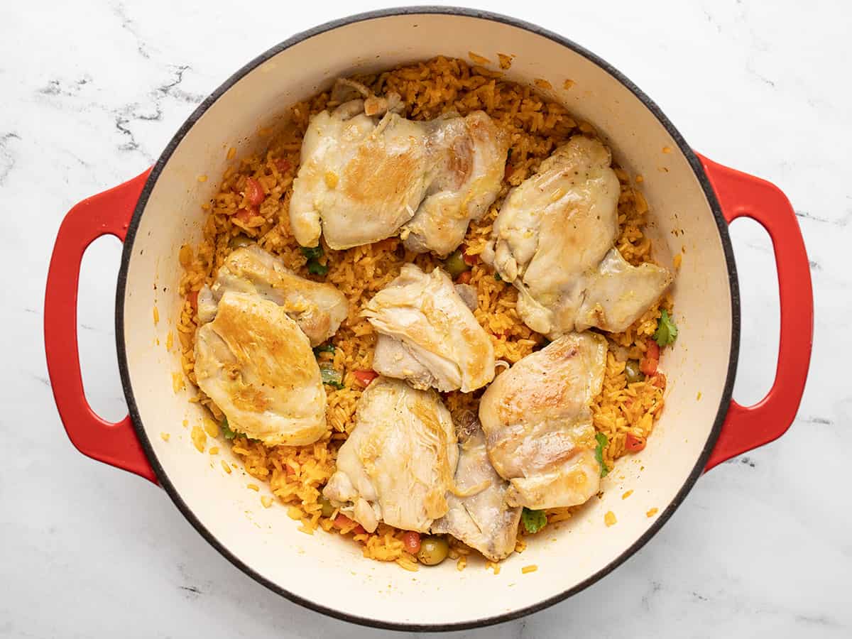 Rice topped with chicken in a red Dutch oven.